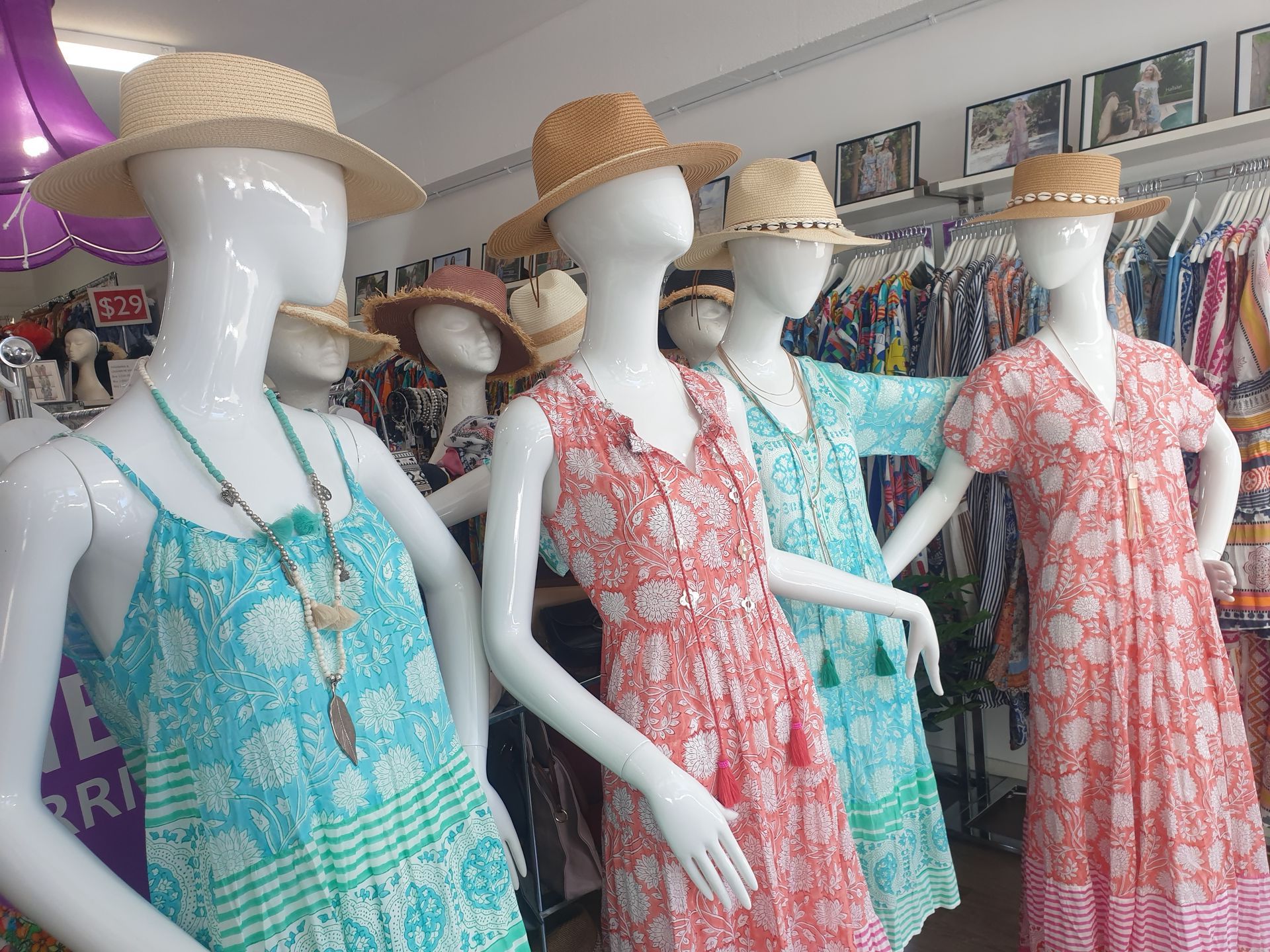 Mannequins wearing colorful summer dresses and straw hats in a retail store.