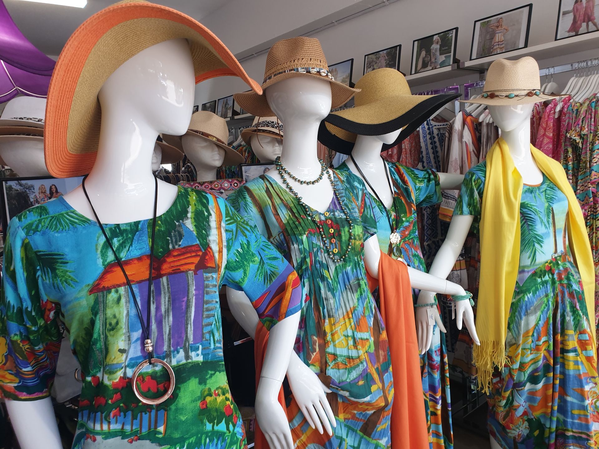 Mannequins in a store window display wearing colorful tropical dresses and hats.