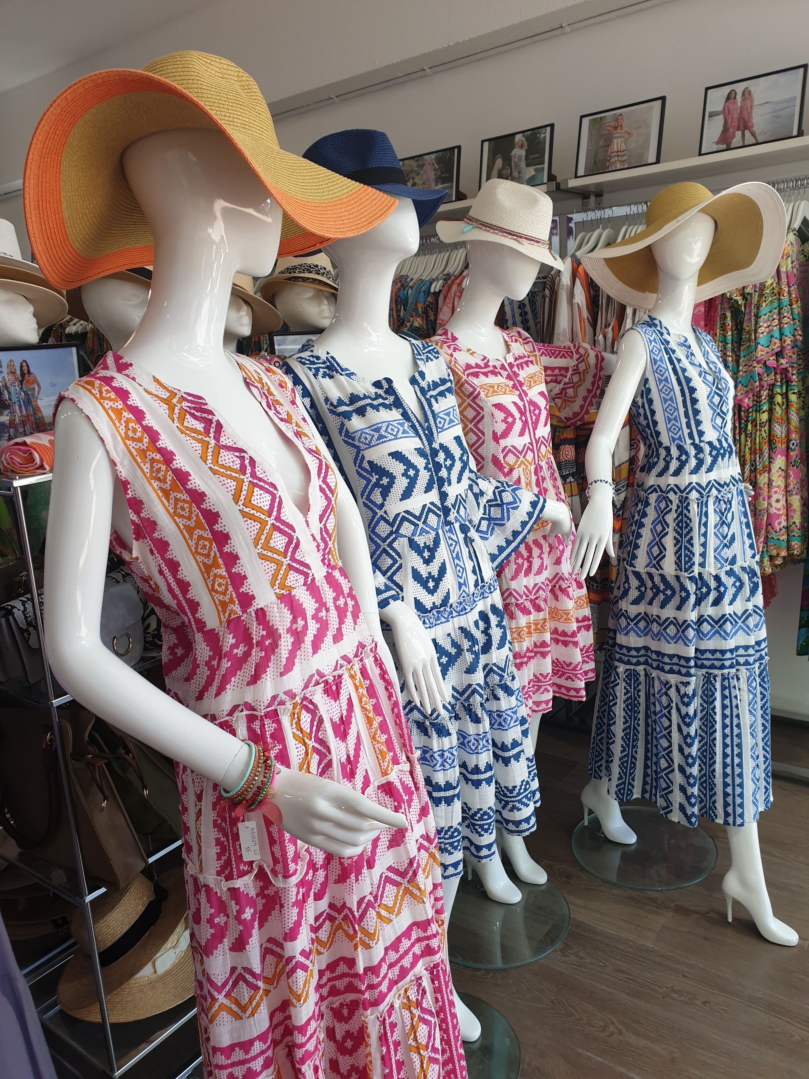 Mannequins wearing colorful summer dresses and hats, in a clothing store.