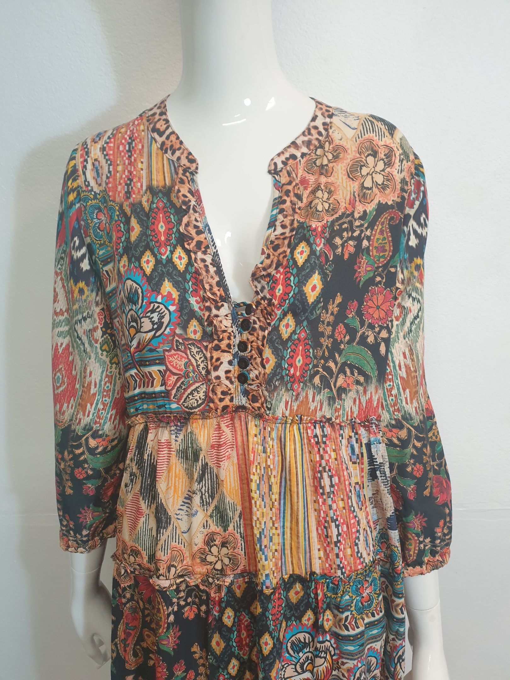 Womannequin wearing a multi-colored patterned dress with a plunging neckline and long sleeves.