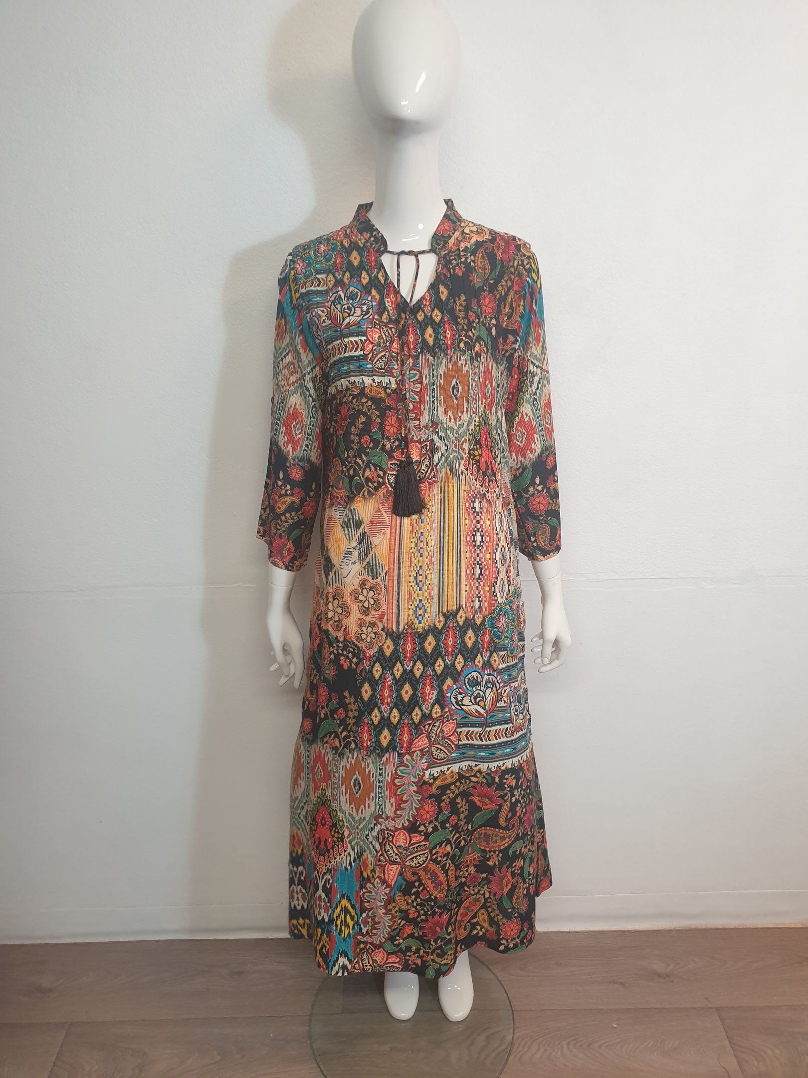 A long, patterned dress with long sleeves on a mannequin; in a light-filled room.