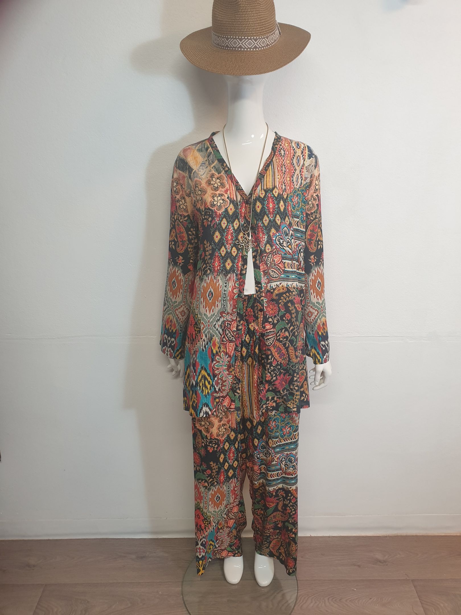 Mannequin wearing a floral patterned outfit, straw hat, and beaded necklace.