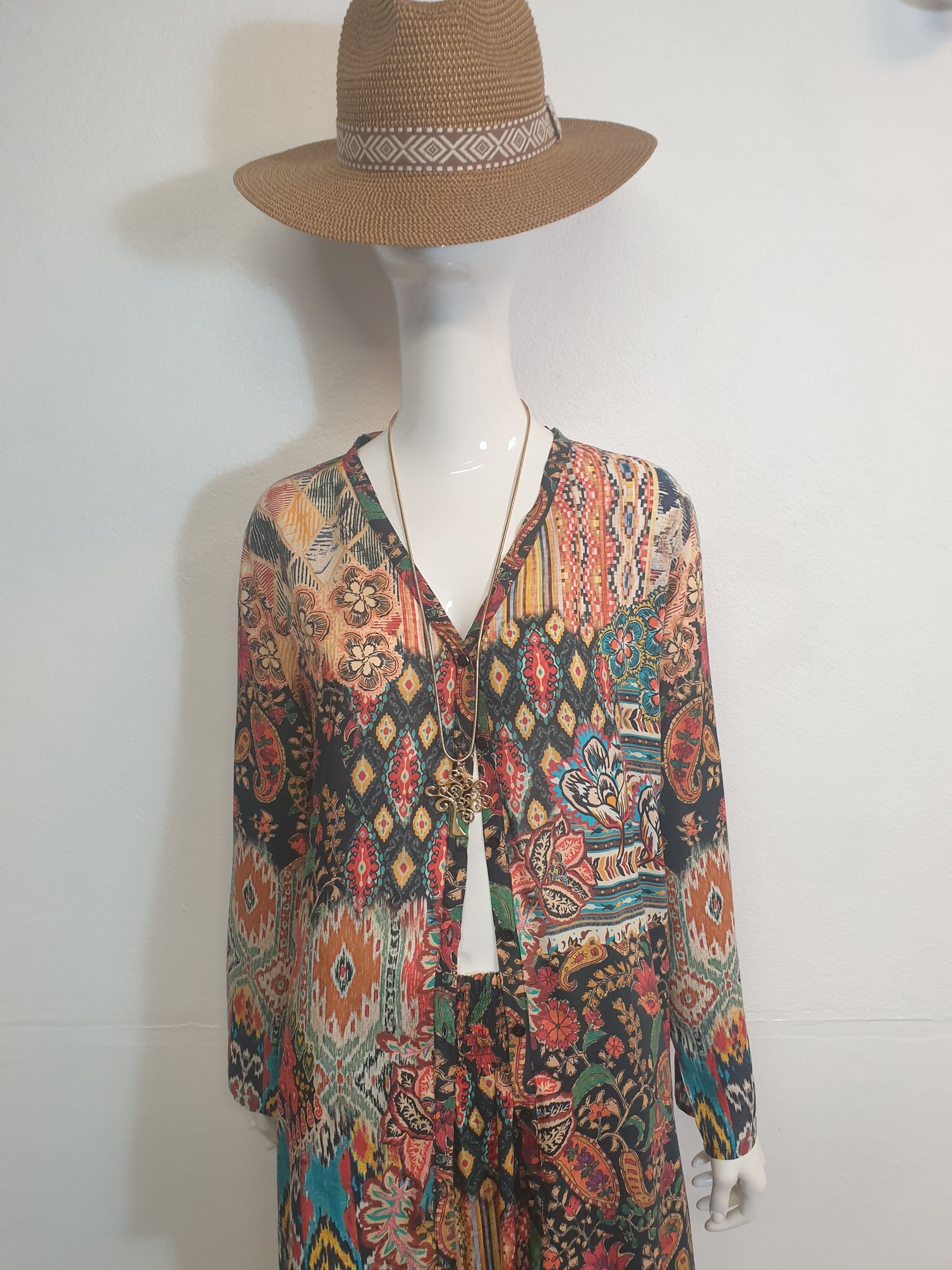 Mannequin wearing patterned dress, straw hat, and necklace.