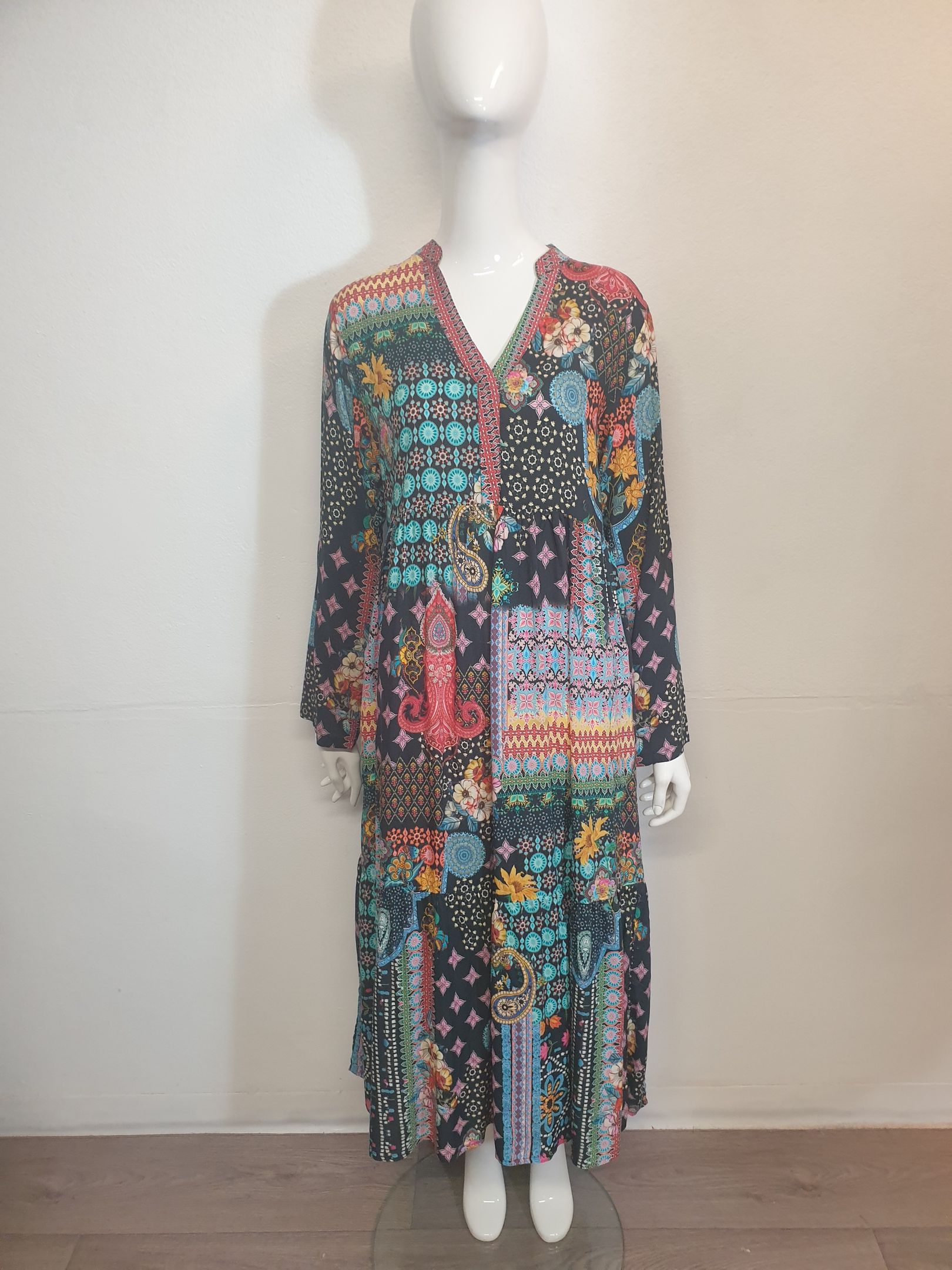 Mannequin wearing a long, patterned dress with a v-neck. The dress features various colorful designs on a dark background.