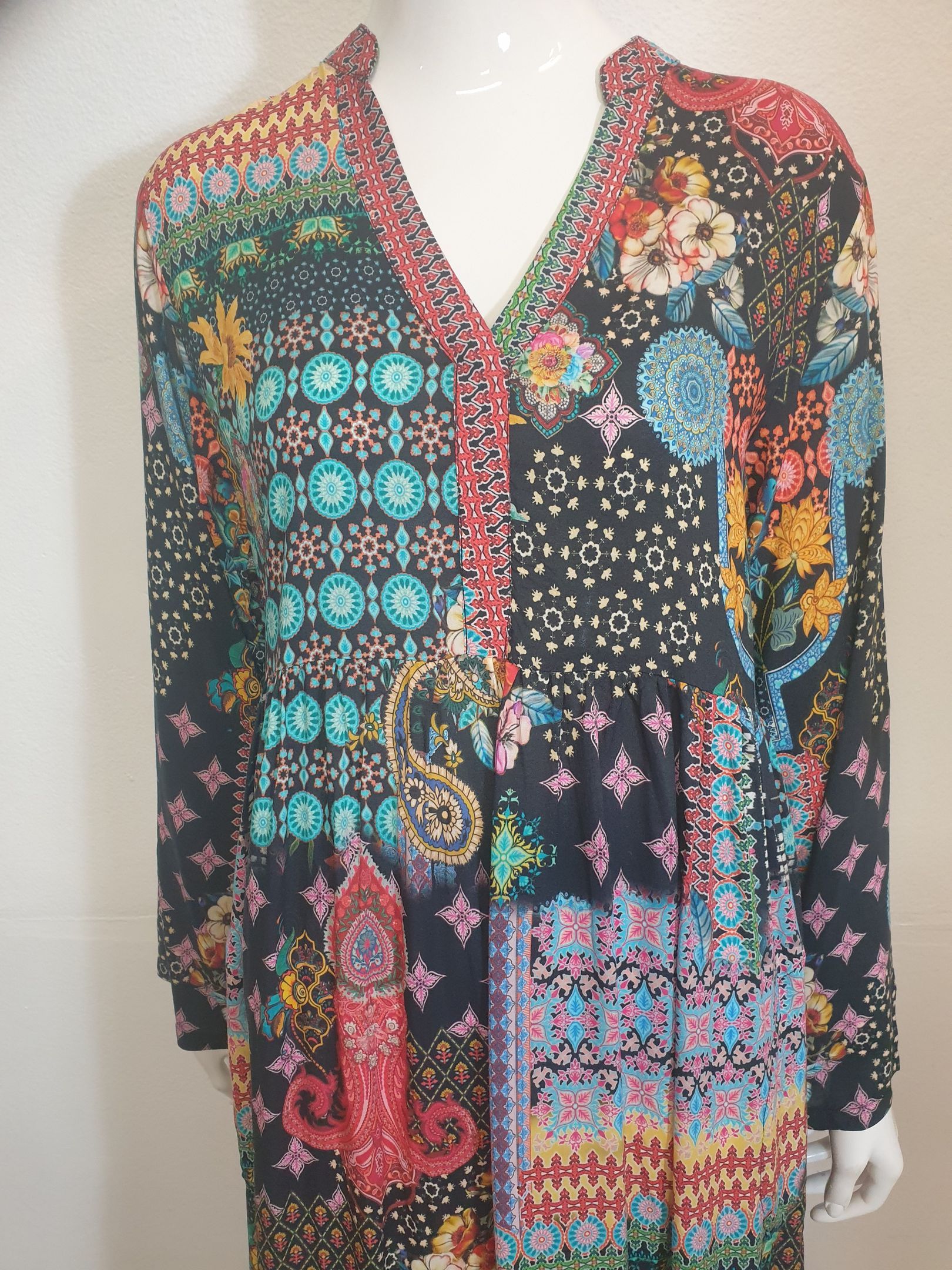 Colorful patterned long-sleeve dress on a mannequin; floral, paisley, and geometric designs in various colors.