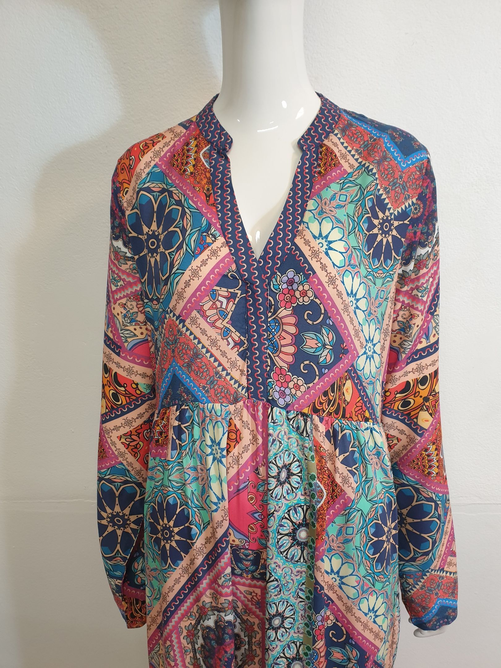Colorful patterned dress on a mannequin; long sleeves, v-neck with decorative trim.