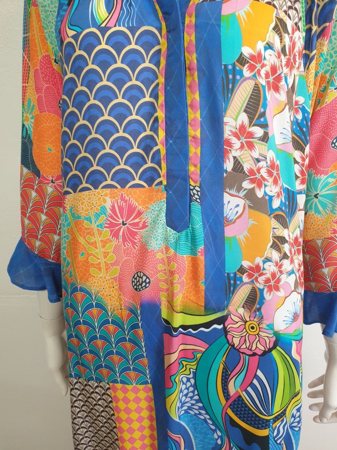 Colorful patchwork tunic with floral, geometric, and abstract patterns; blue ruffled sleeves.