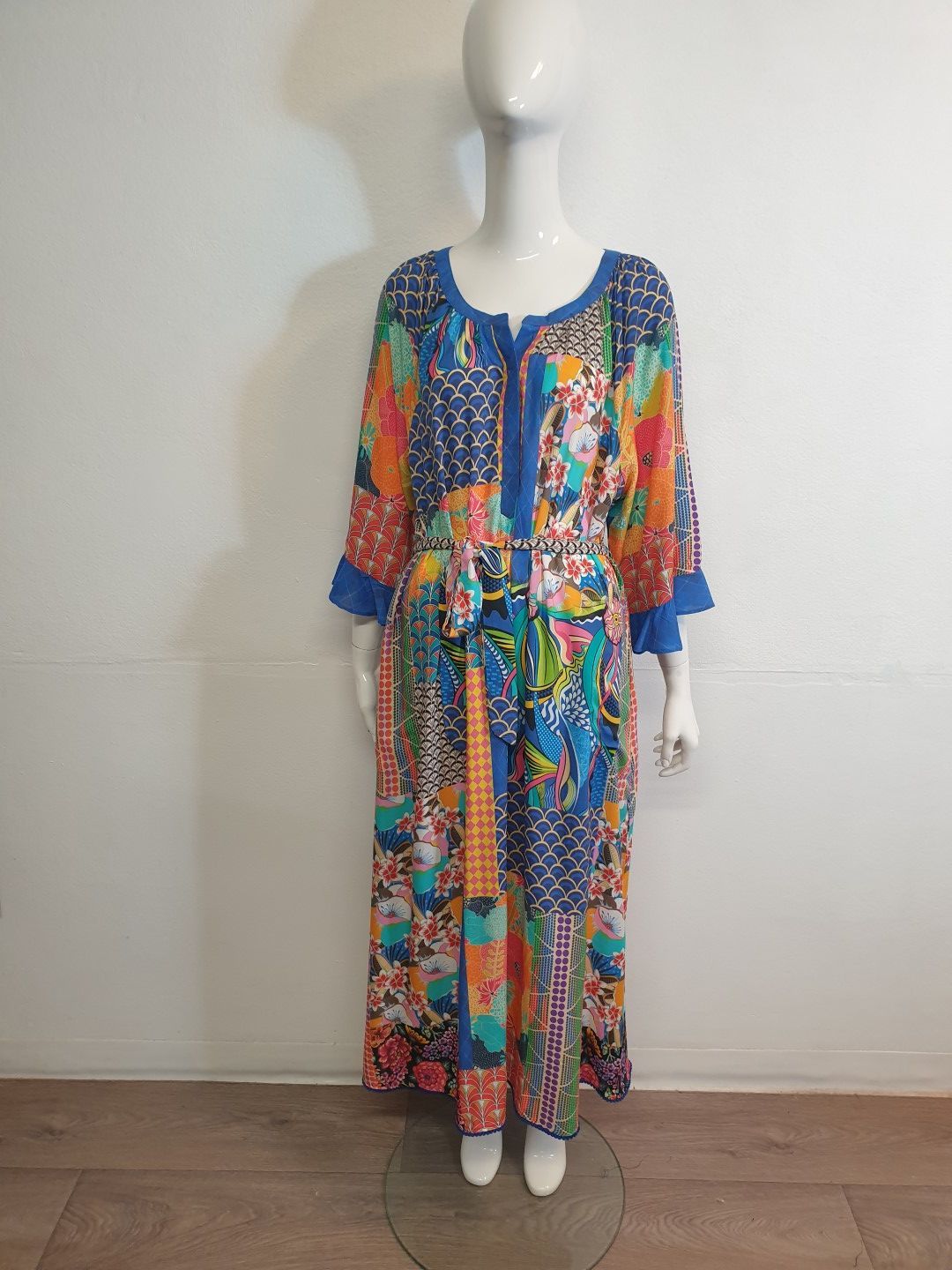 Mannequin wearing a long, colorful patchwork print dress with blue trim and belt.