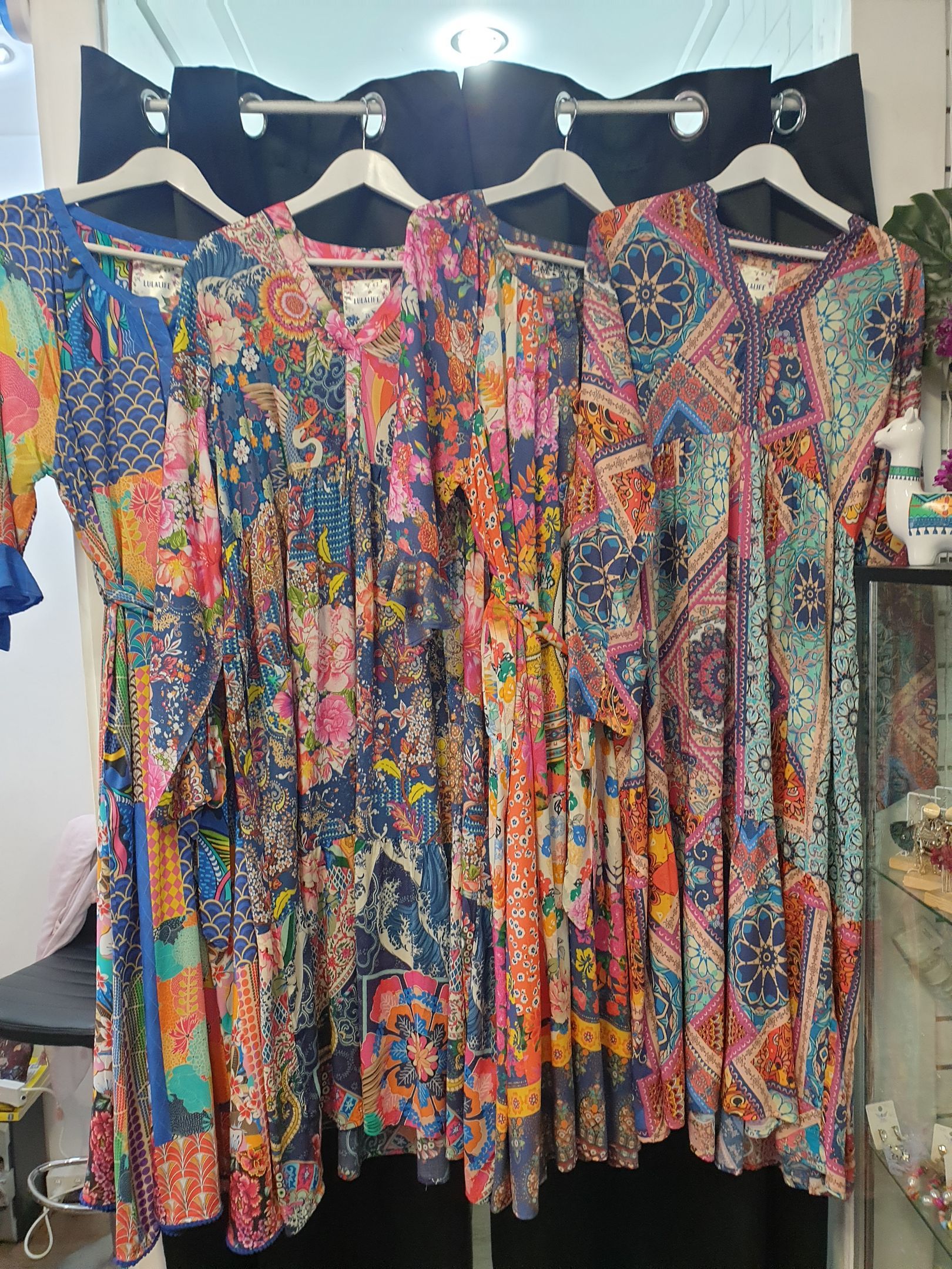 Five colorful patterned dresses hanging on display in a store.