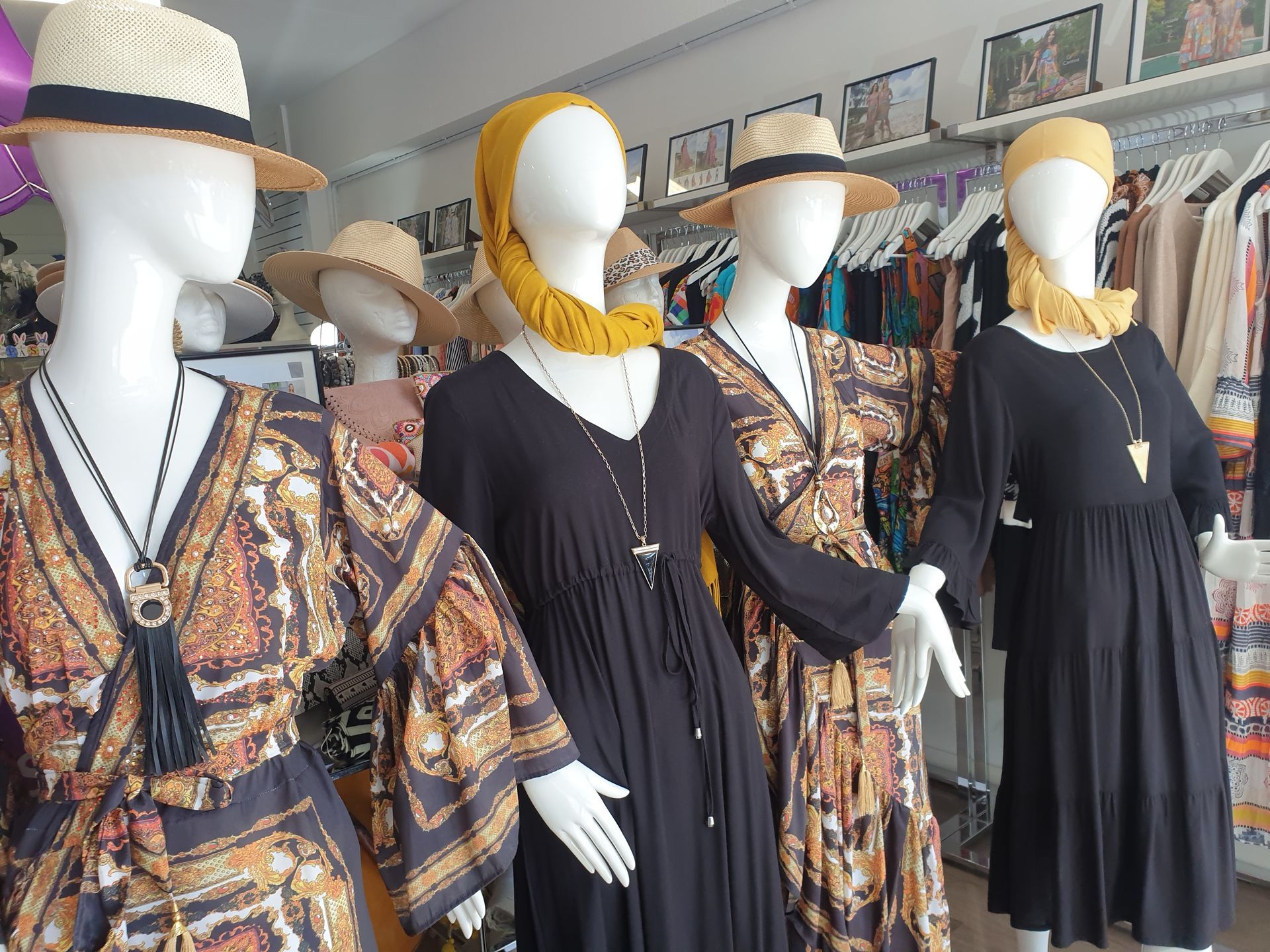 Mannequins in a clothing store wearing dresses and hats; mostly black and patterned garments.