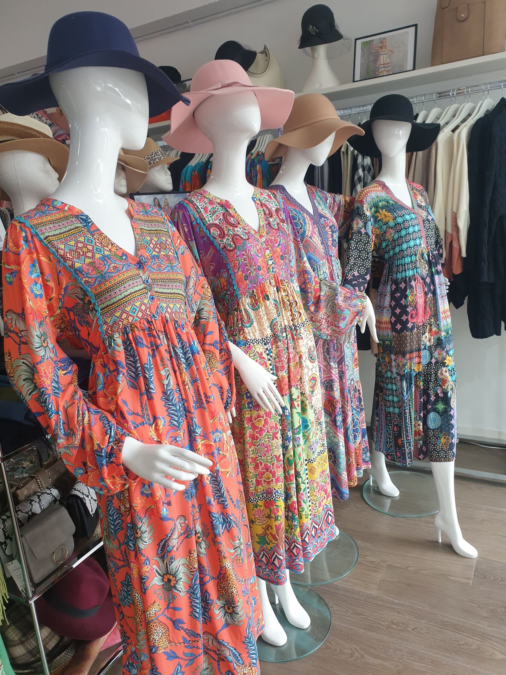 Mannequins wearing floral dresses and hats in a clothing store.