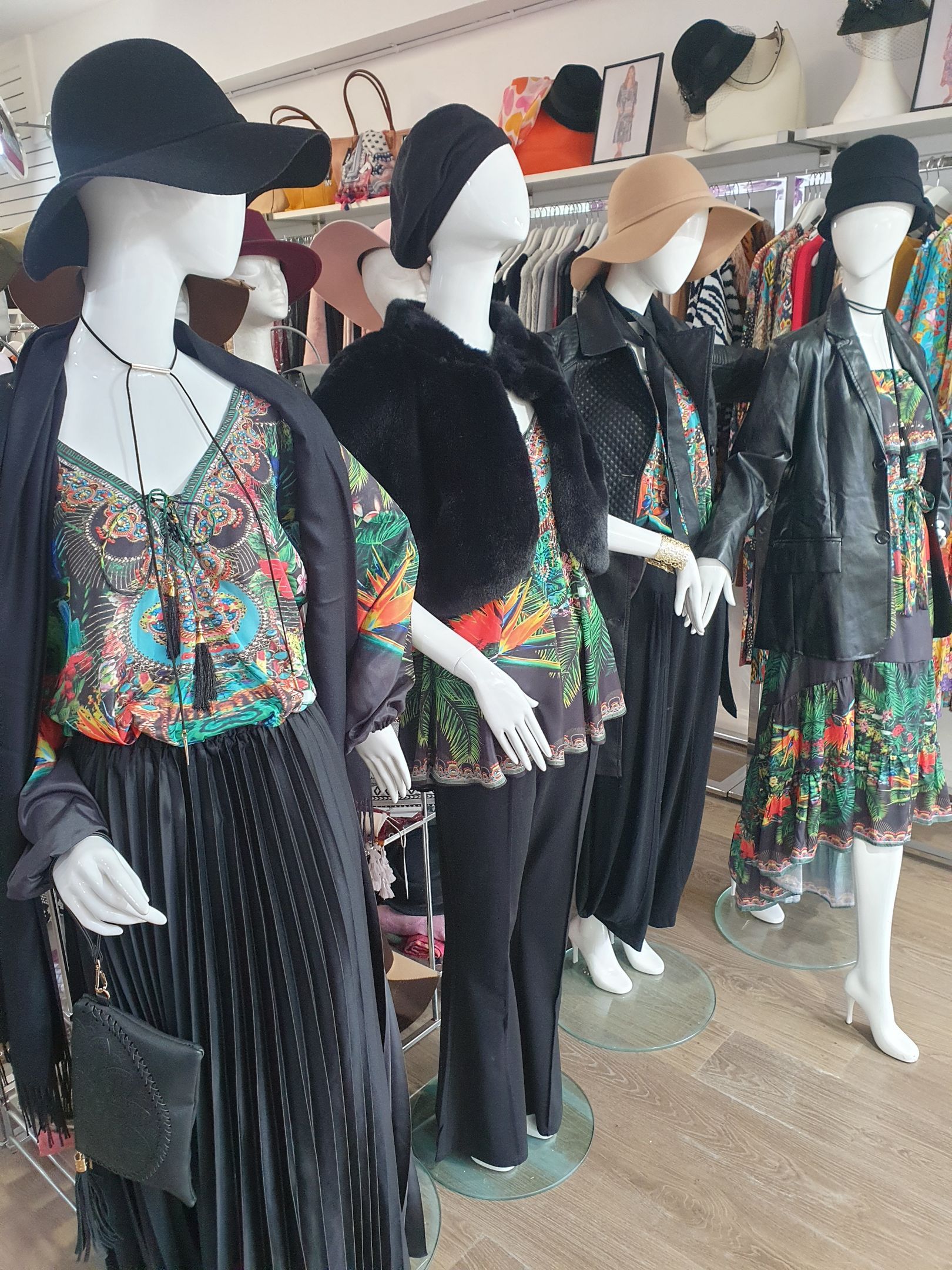 Mannequins in a clothing store, wearing outfits with floral patterns, hats, and black jackets.