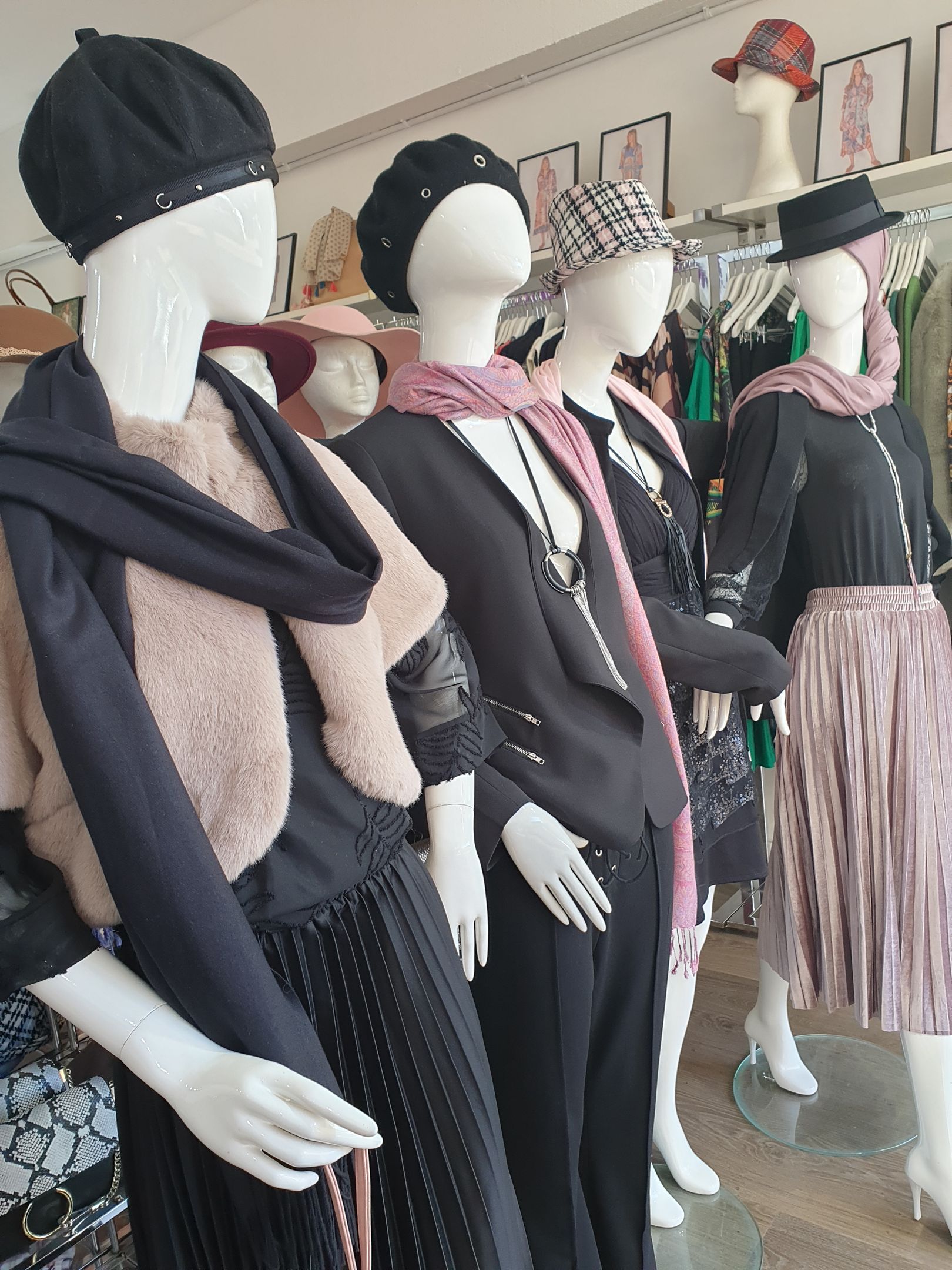 Mannequins wearing fashionable hats, scarves, jackets, and skirts in a shop display.
