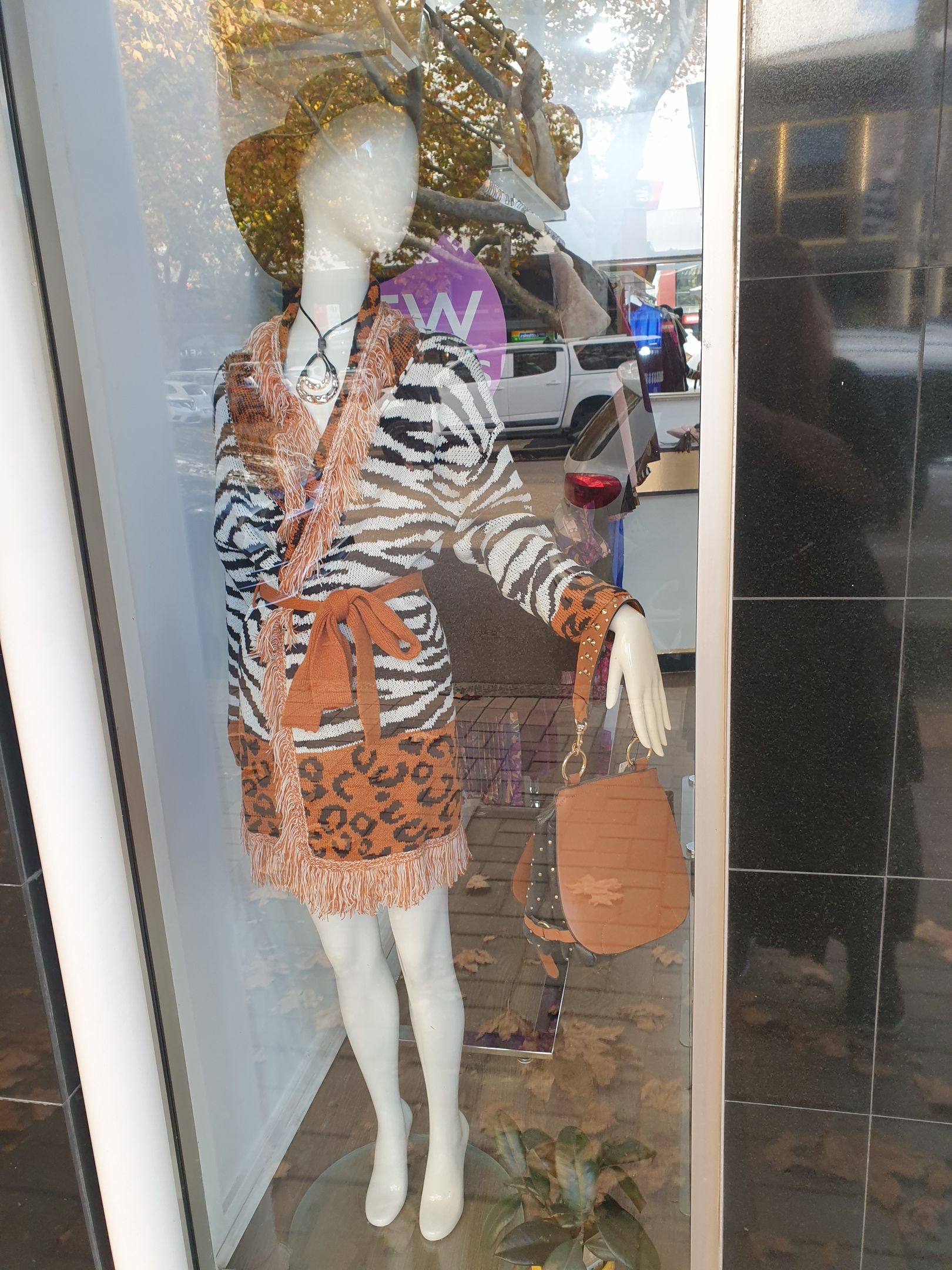 Mannequin in window display, wearing zebra print coat dress and carrying purse.