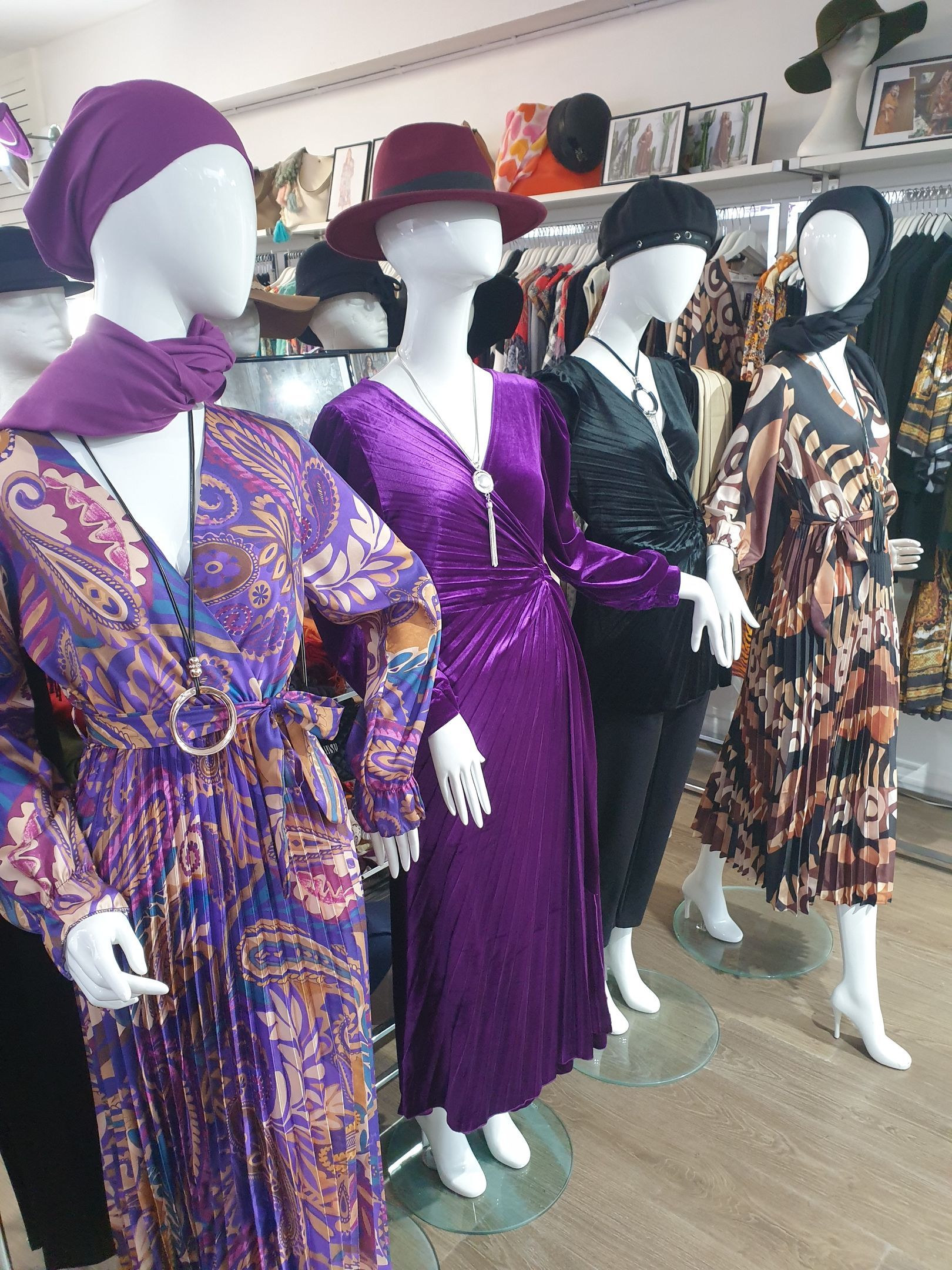 Five mannequins wearing colorful clothing and hats in a clothing store.