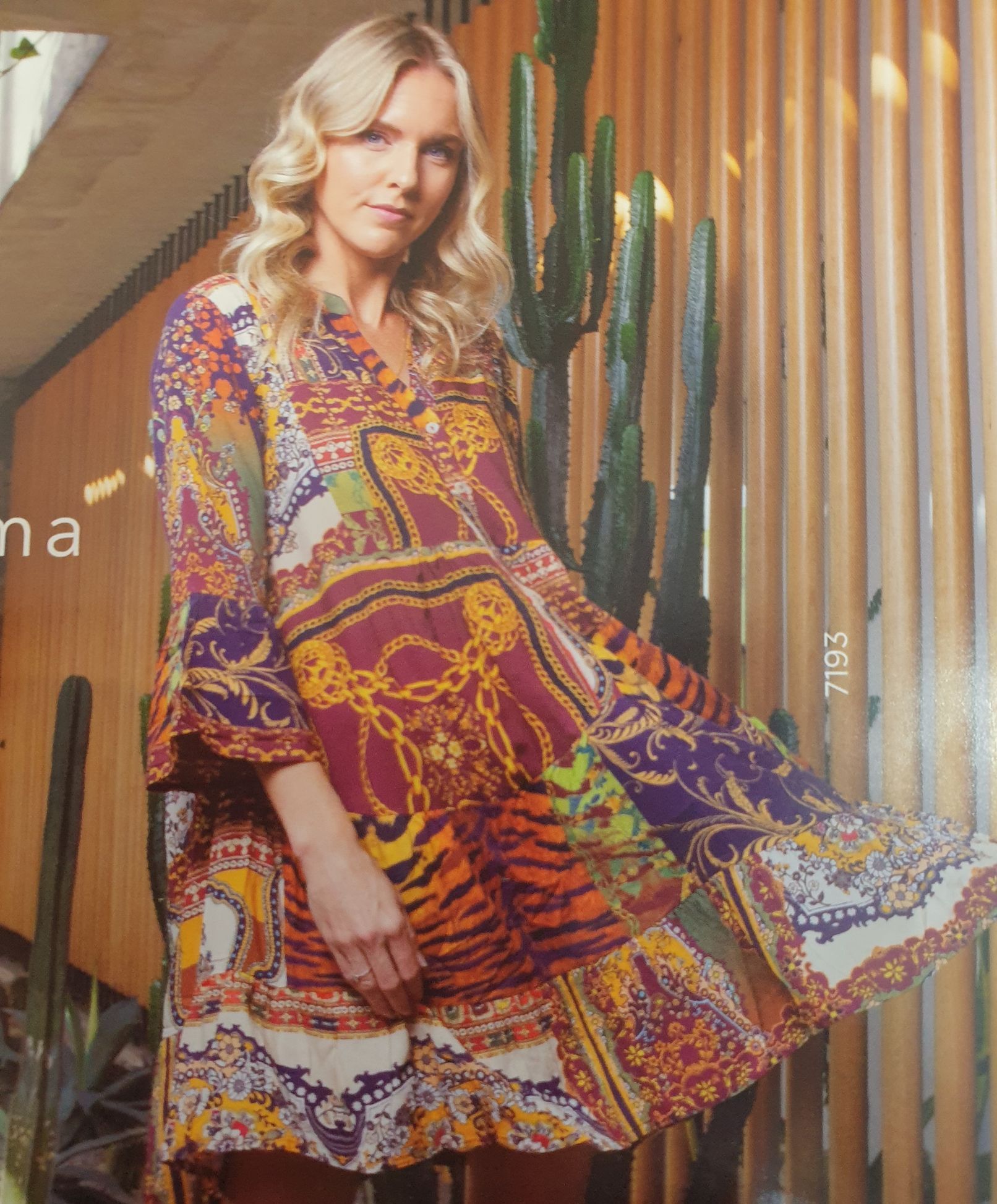 Woman wearing a colorful patterned tunic, standing in front of a wooden wall and cacti.