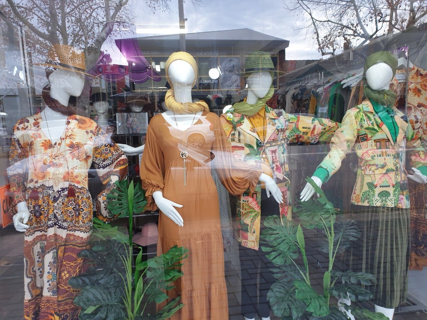 Clothing store window with mannequins in colorful outfits.
