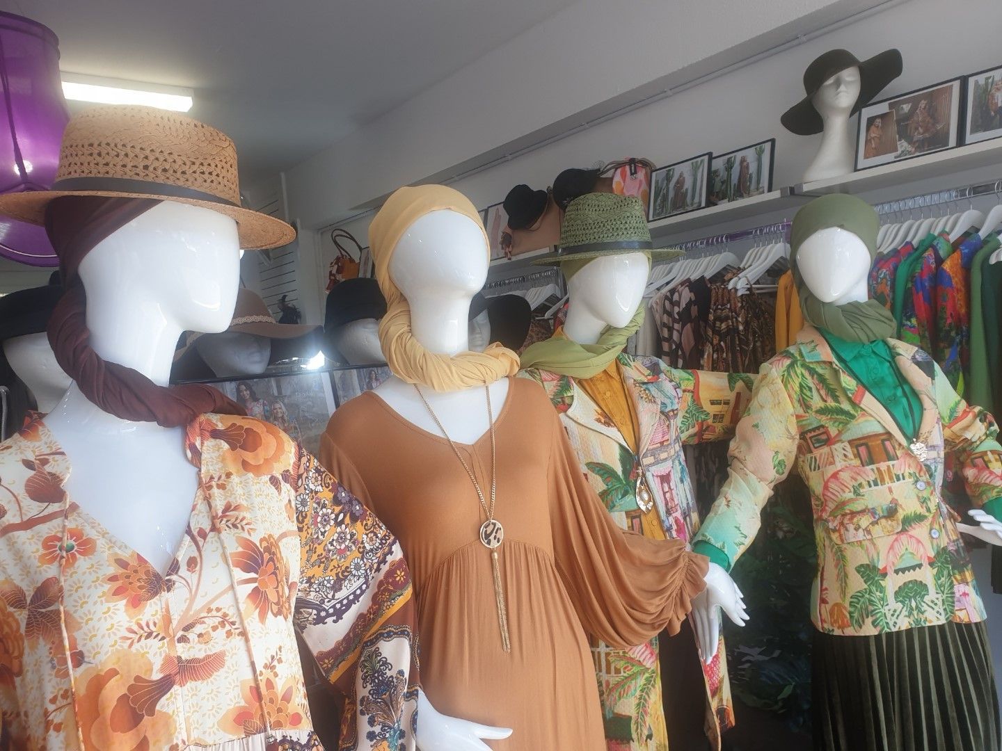 Mannequins in a clothing store display boho-style outfits: dresses, jackets, hats, and scarves in earthy tones.