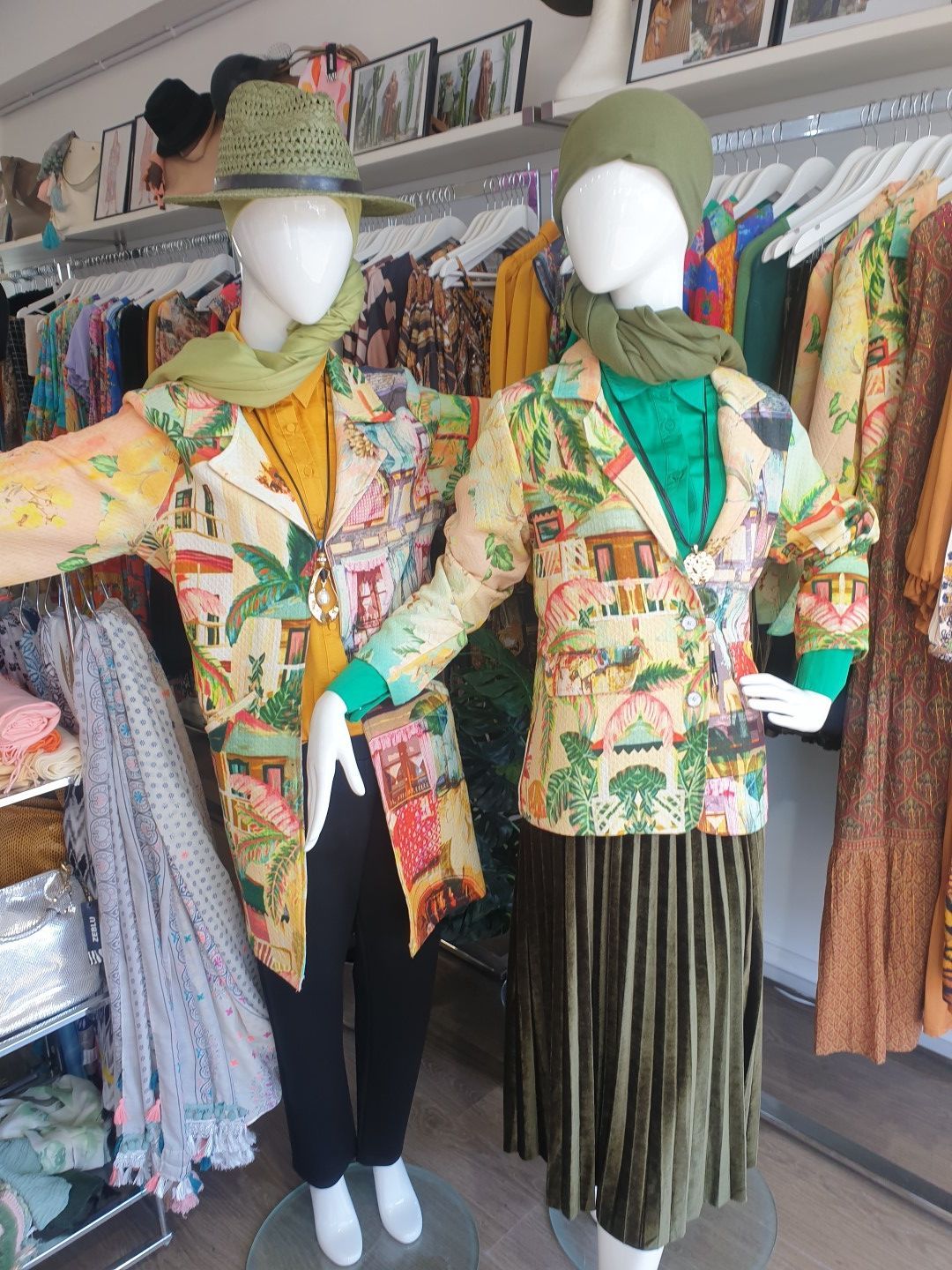 Two mannequins in a clothing store, wearing colorful patterned jackets, scarves, and hats.