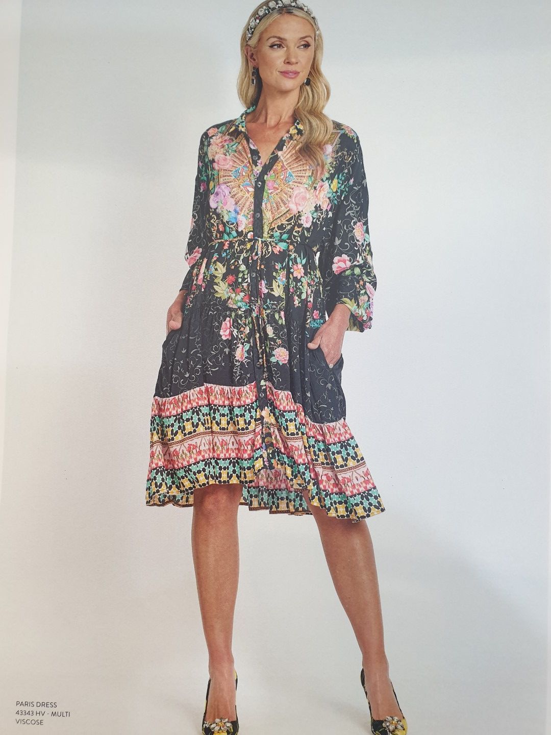 Woman in a black floral dress with a headband, holding a pose against a white background.