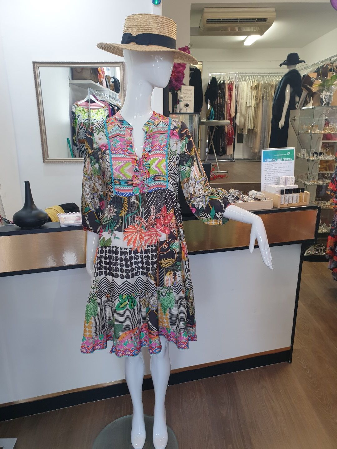Mannequin in a colorful printed dress and straw hat inside a clothing boutique.