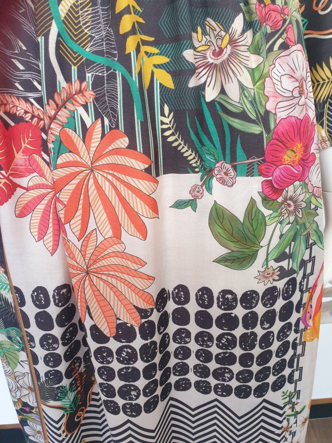 Close-up of patterned fabric with large orange and pink flowers, black and white geometric shapes, and foliage.