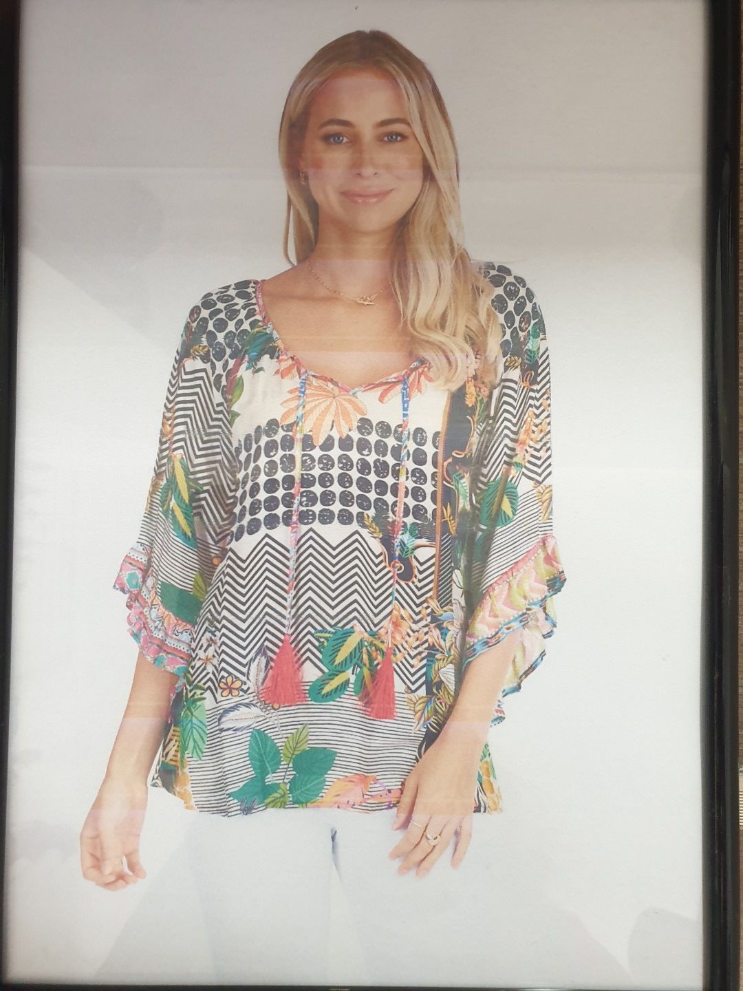 Woman in a floral top and white pants, smiling.