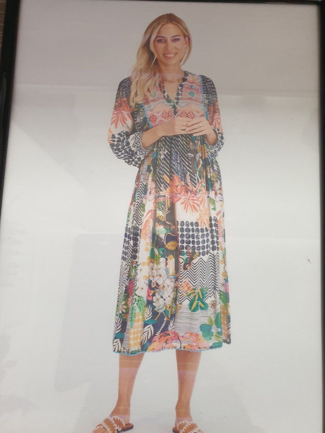 Woman in floral patchwork midi dress, standing with hands clasped, smiling.