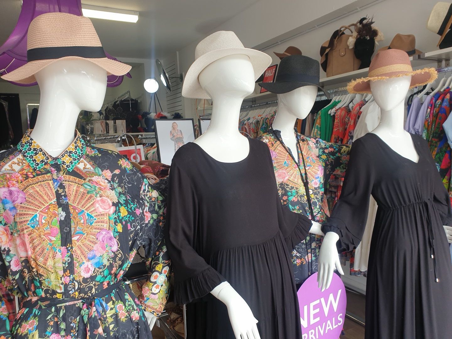 Four mannequins in a shop window, wearing dresses and hats. Floral and black dresses displayed; 