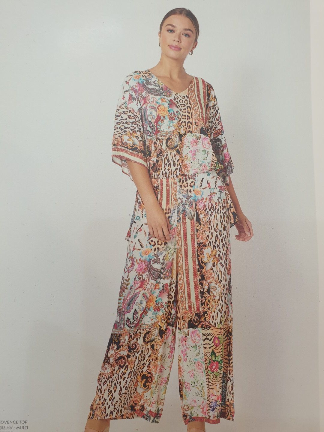 Woman wearing a colorful floral and animal print jumpsuit, standing indoors.