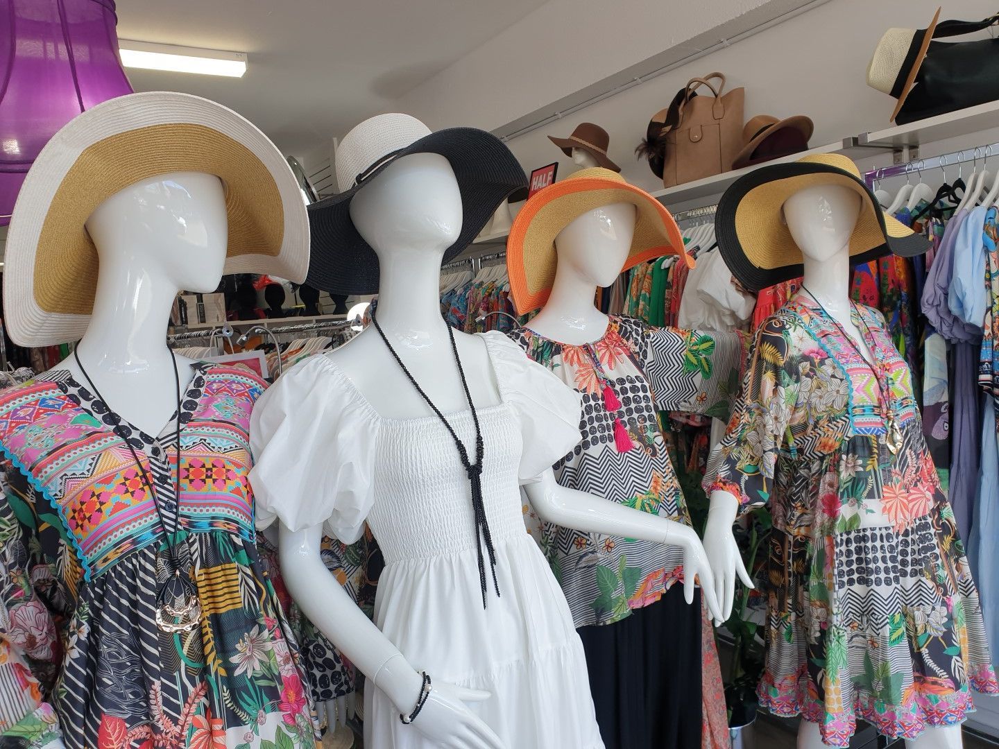 Four mannequins wearing hats and colorful summer clothing in a boutique.