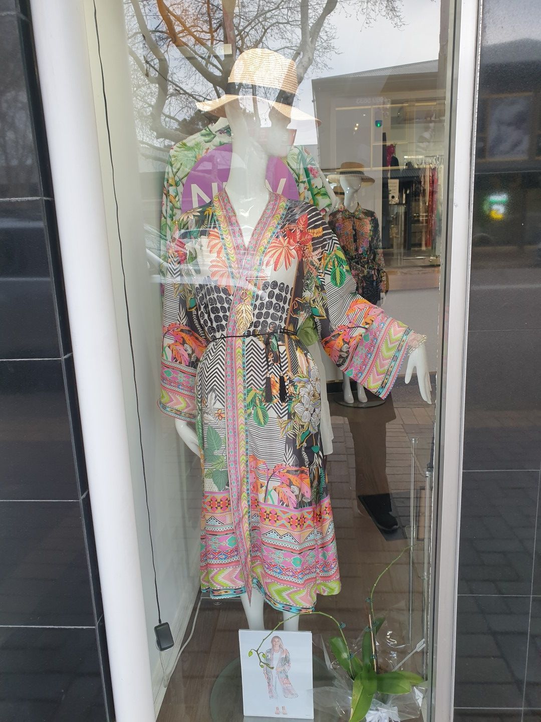 Mannequin in a window display wearing a colorful patterned robe, straw hat, and a sketch.