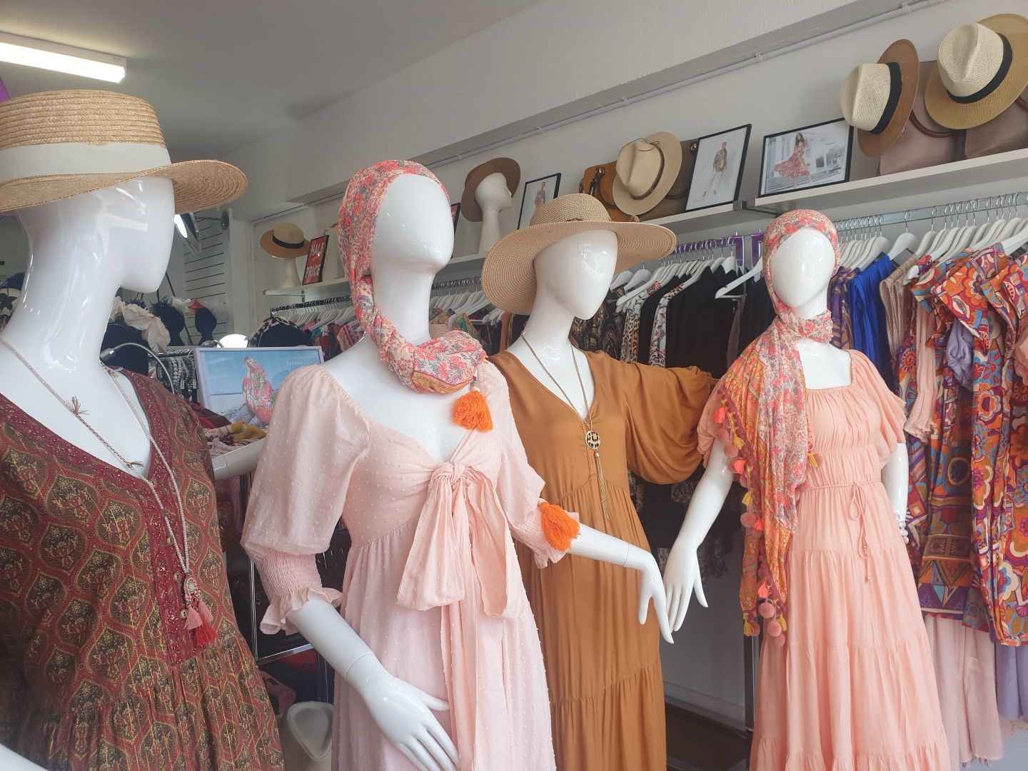 Four mannequins in a clothing store, wearing dresses, hats, and scarves. Soft colors, hats on display.