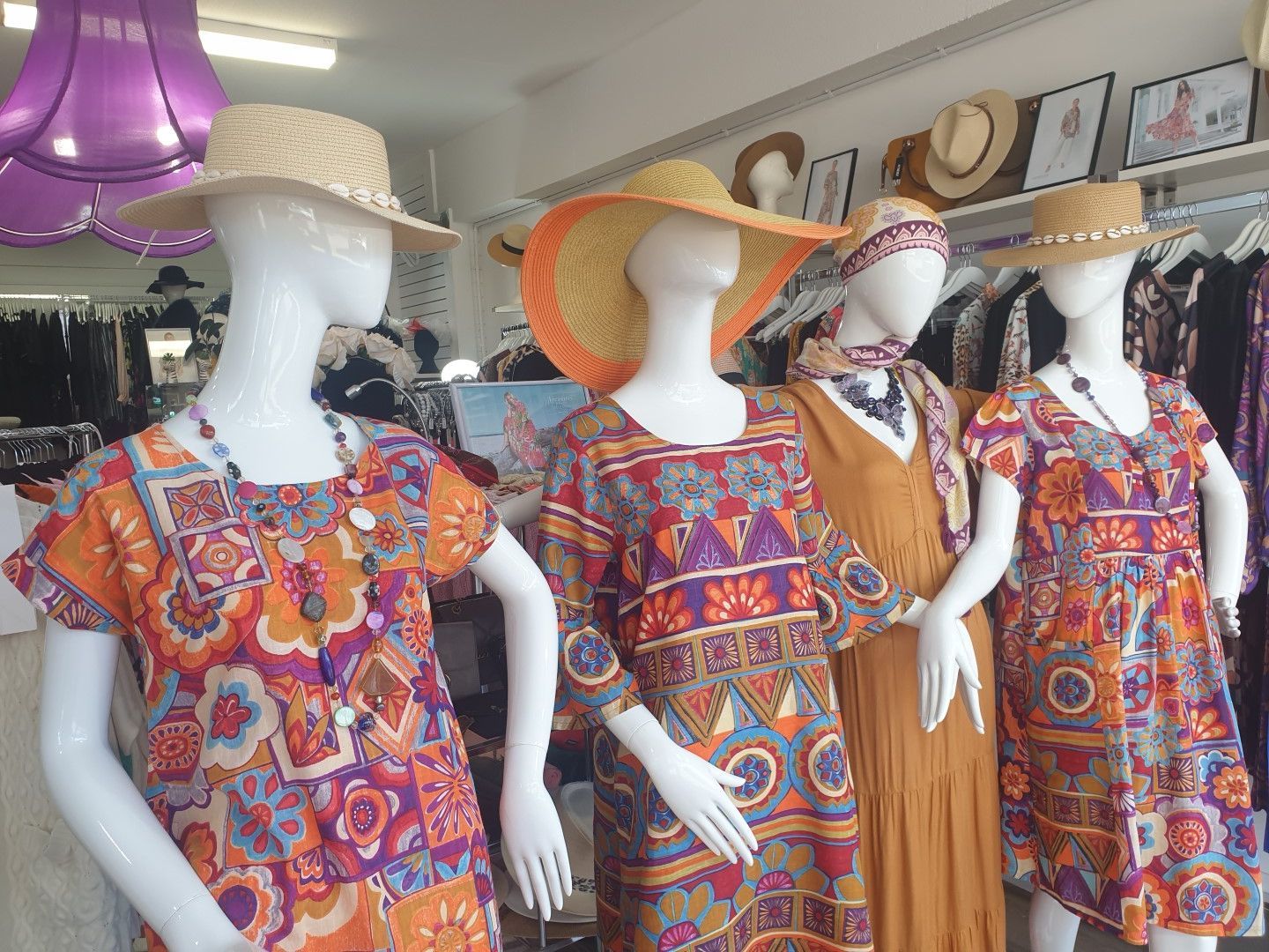 Four mannequins in a shop window display colorful summer dresses and hats.