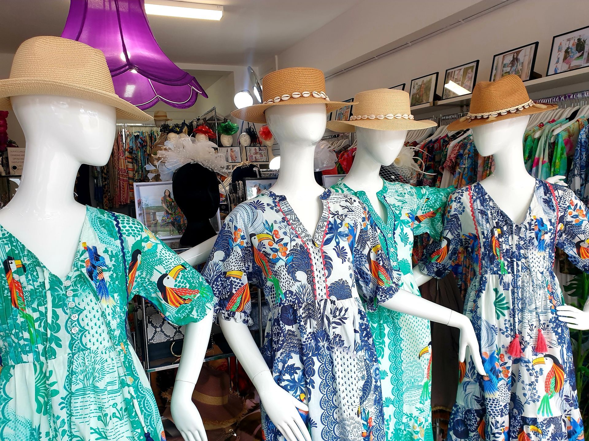 Mannequins wearing patterned dresses and straw hats in a store.