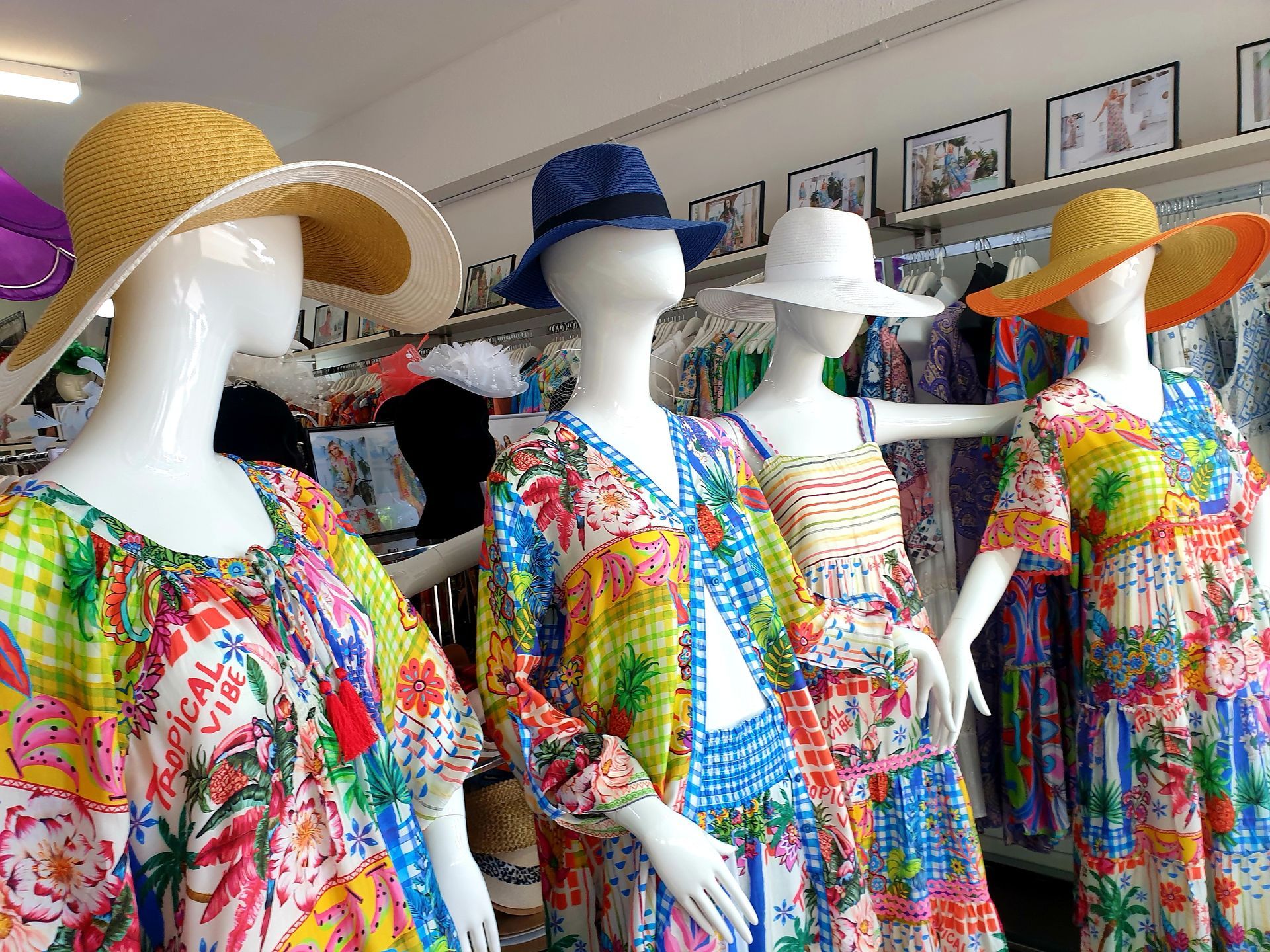 Mannequins in a shop window display colorful summer dresses and hats.