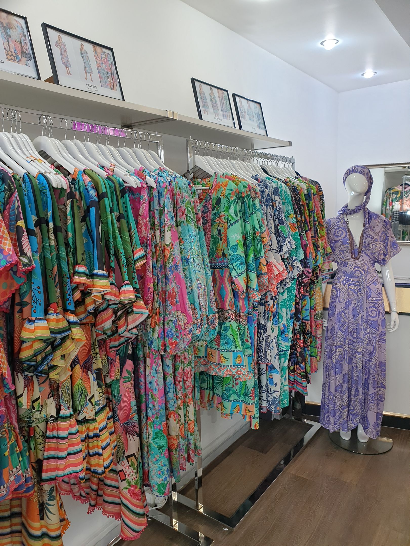 Colorful patterned dresses hanging on a rack in a clothing store, a mannequin wears a purple dress.