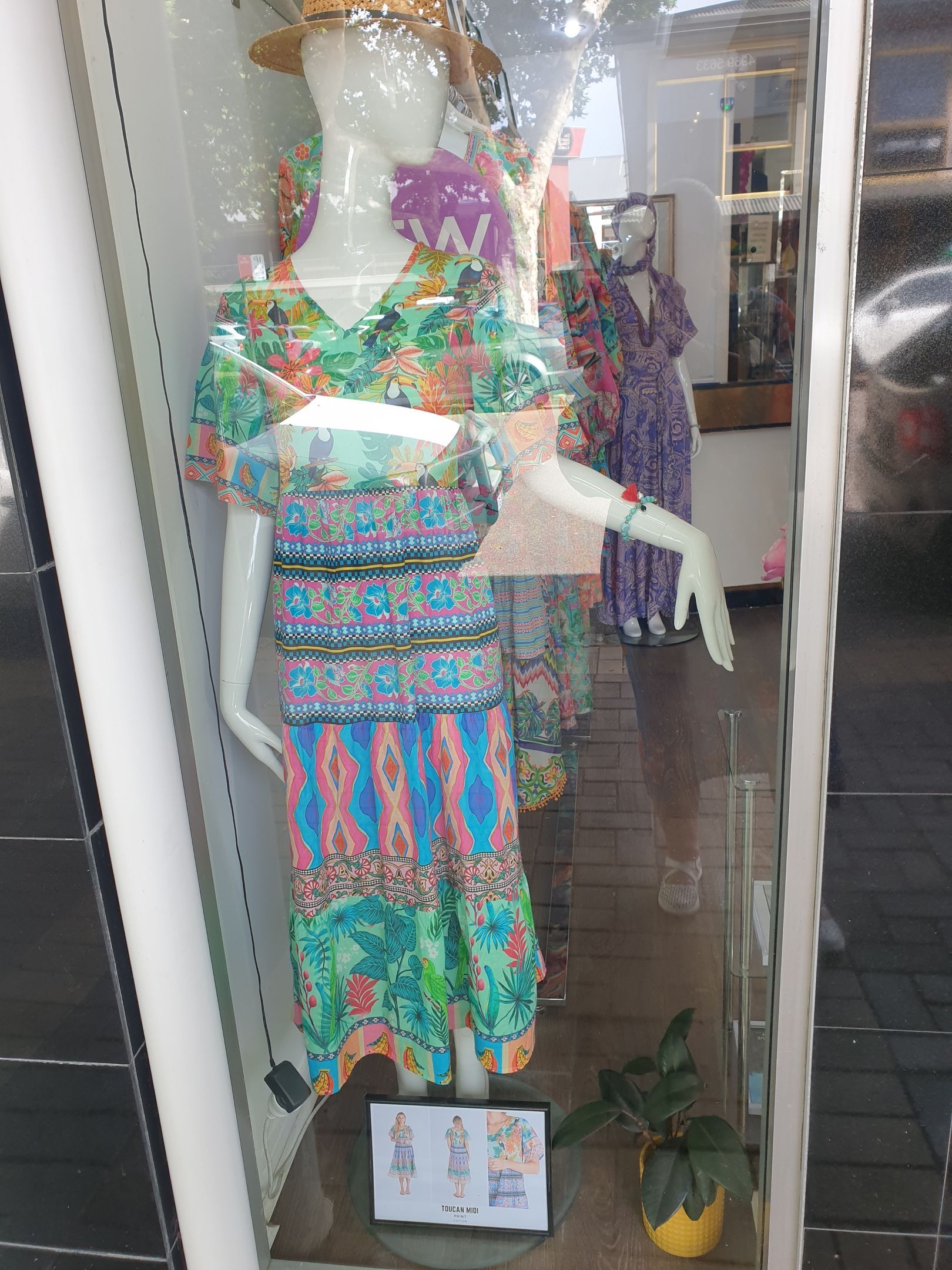 Mannequin in a window display, wearing a colorful floral dress and straw hat.