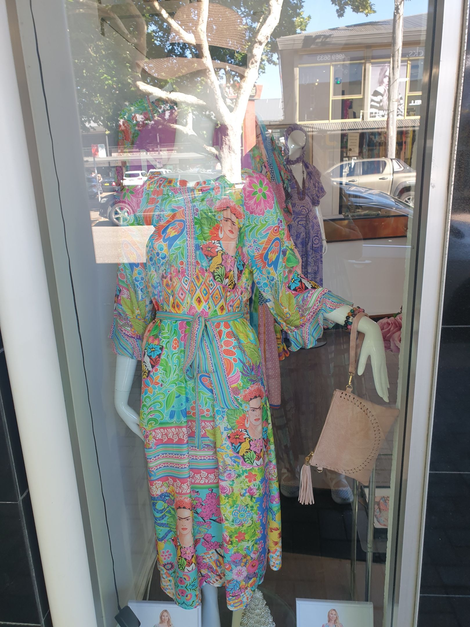 Woman's dress in a storefront display. Colorful floral print dress on a mannequin, holding a purse.