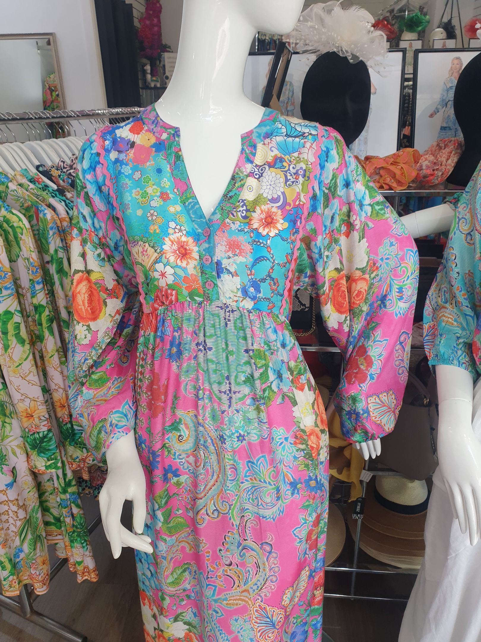 Mannequin in floral print dress, pink, blue, orange, V-neck, long sleeves, fitted waist, display in a store.