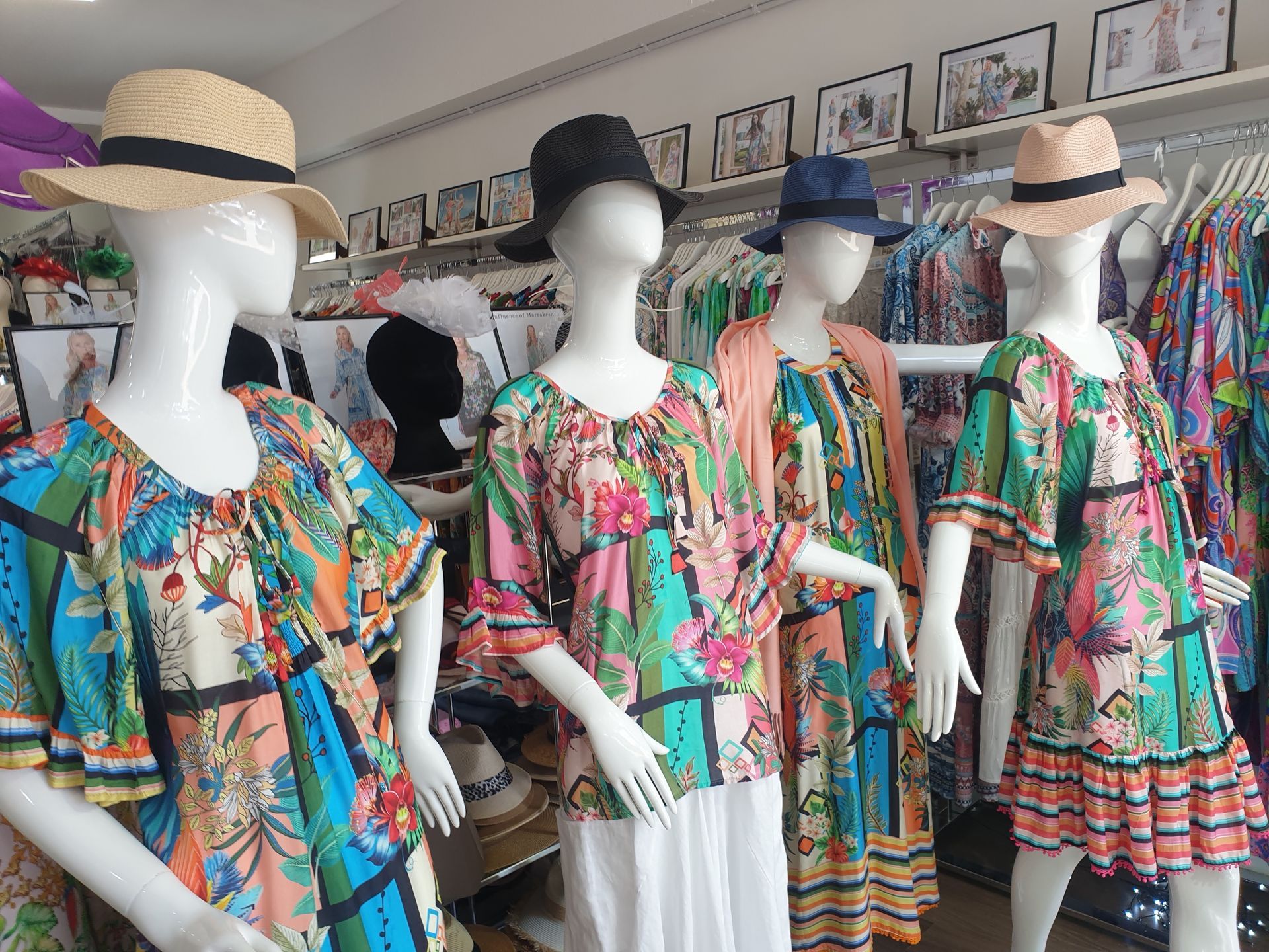 Four mannequins in a clothing store, wearing colorful floral print tops and dresses, and straw hats.