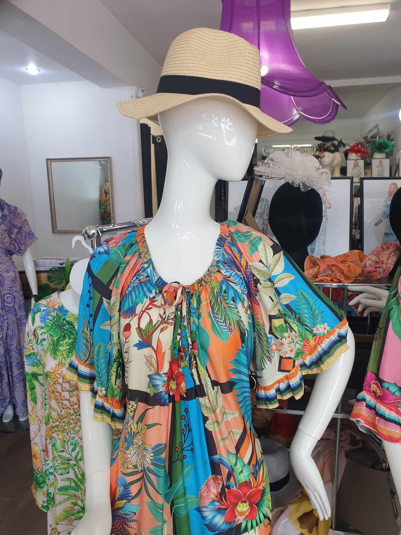 Mannequin wearing a colorful floral dress and straw hat in a clothing store.
