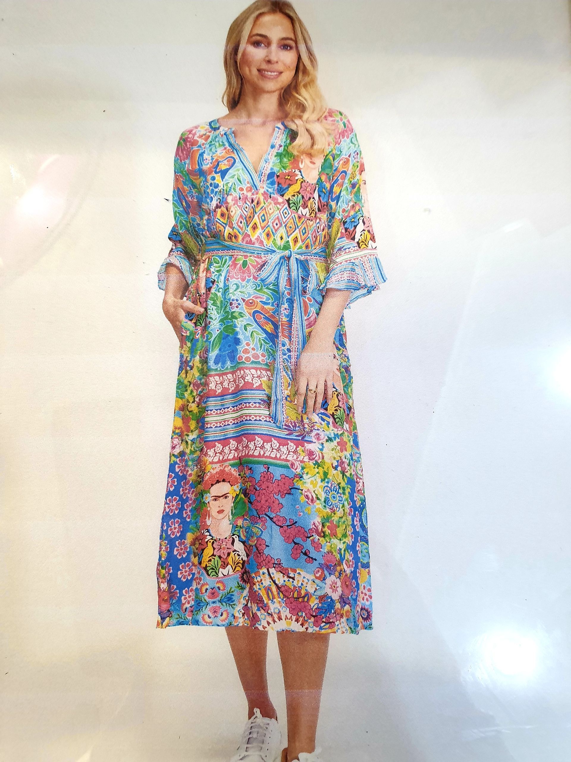 Woman in a colorful patterned dress with sleeves and a waist tie, posing against a white background.