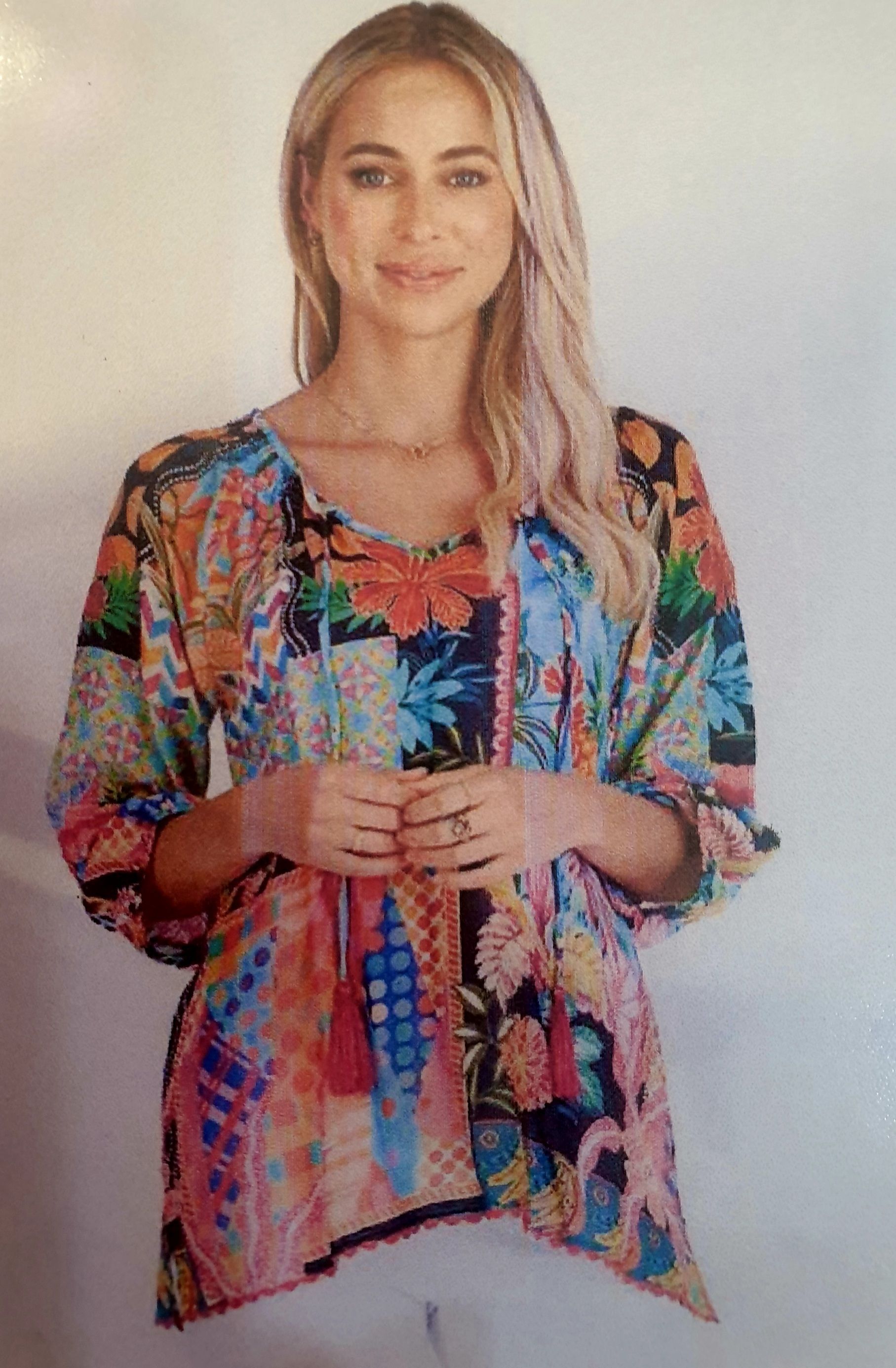 Woman in colorful patchwork top, hands clasped.