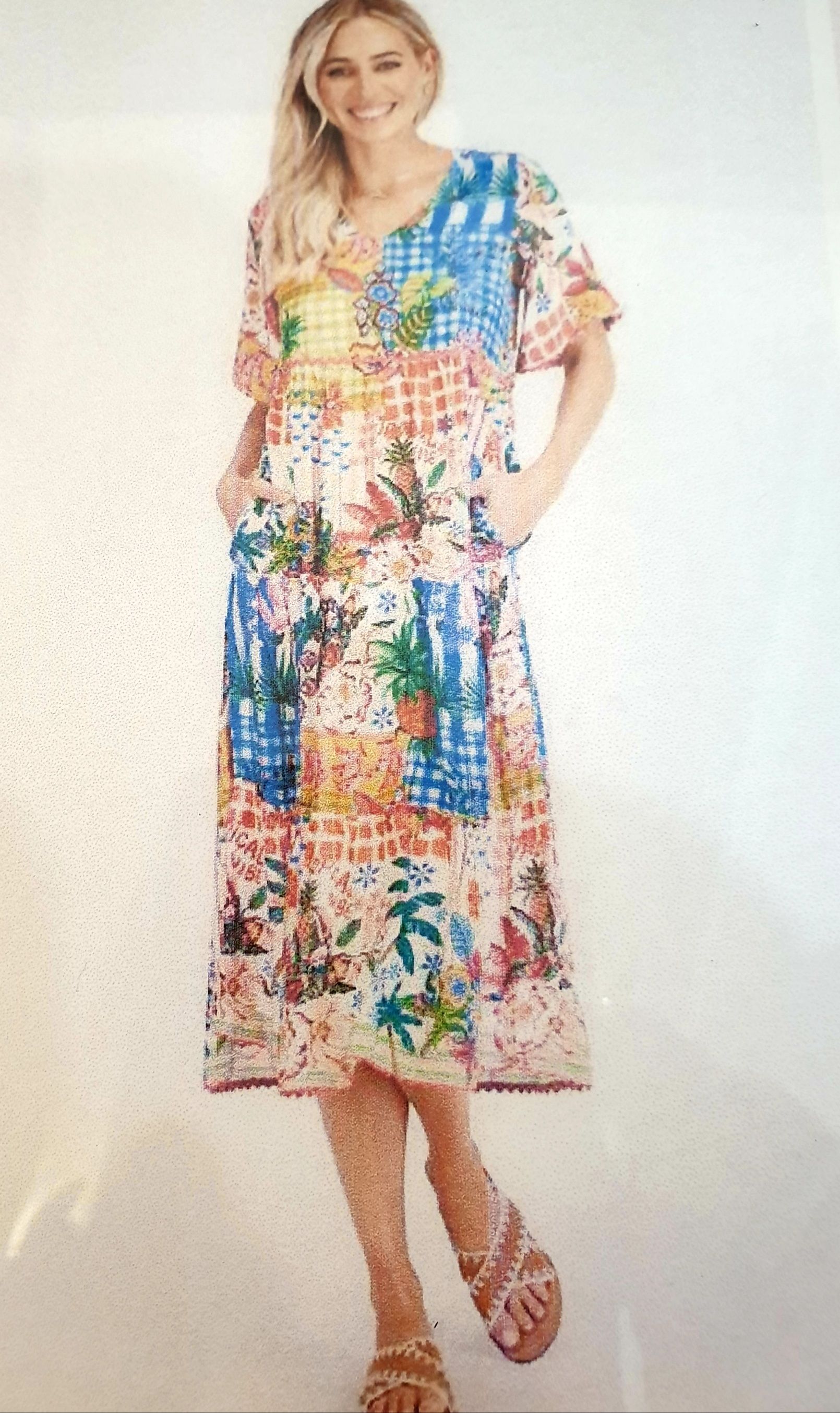 Woman wearing a patchwork floral dress with pockets, smiling, standing outdoors.