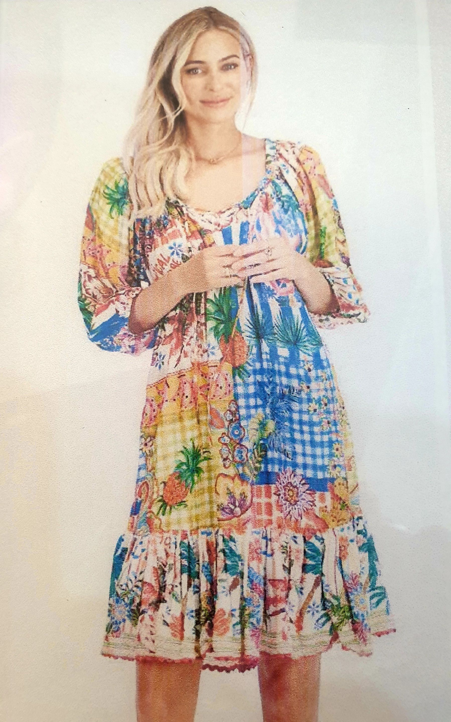 Woman in floral patchwork dress smiles, outdoors.