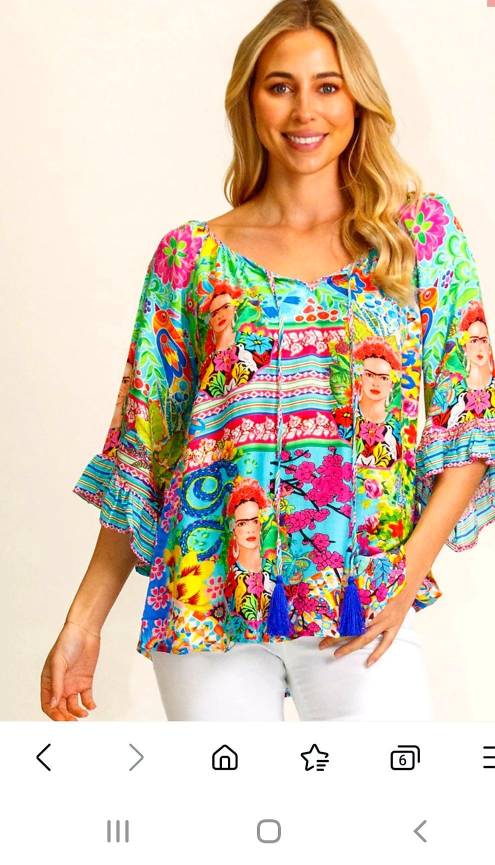 Woman in colorful Frida Kahlo print top, white pants, smiling.