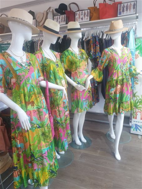 Four mannequins in a store wearing colorful floral dresses and straw hats.