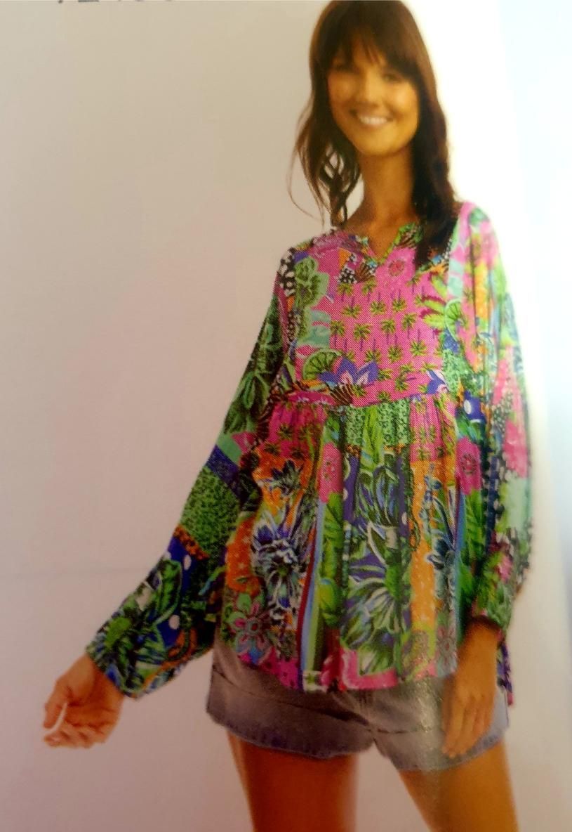 Woman in colorful floral top and denim shorts, smiling, outdoors.