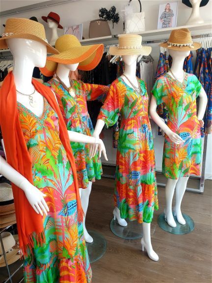 Four mannequins wearing colorful floral dresses and straw hats in a clothing store.